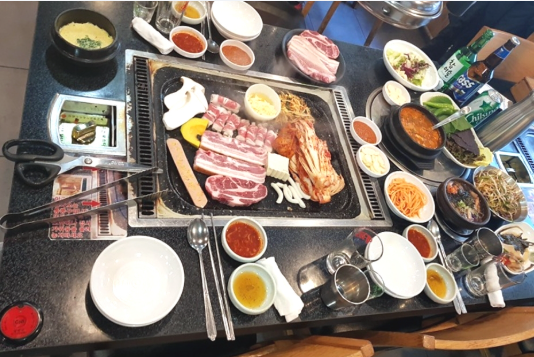 A generous full table layout of Jeju pork BBQ at Tamna Doyaji featuring grilled pork belly and various side dishes